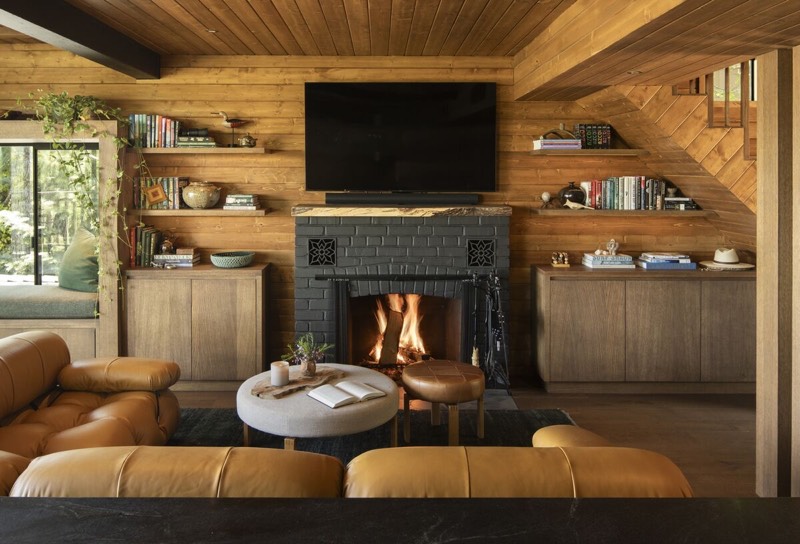 The living room at Little Doe Cabin, with a lit fireplace and wood-clad walls